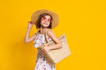 Portrait of happy cheerful girl in summer hat, sunglasses, straw bag over yellow background. 