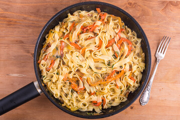 Italian fettuccine pasta with pepper, basil and cream sauce in a frying pan, top view.