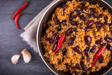 Mexican rice with tomato and beans, serving in a plate with chili peppers, top view.
