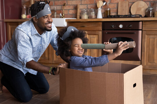 Smiling Loving Young African American Father And Small Biracial Daughter Have Fun Play Pirates Sail In Ship Look In Spyglass. Happy Caring Ethnic Dad Engaged In Playful Activity With Teen Girl Child.