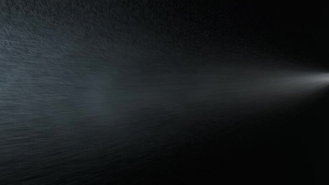 Slow motion. Illuminated jet of droplets on a dark background. Spraying water droplets. Isolated on black background.