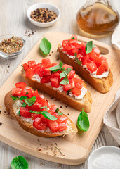 Italian bruschetta with tomato, cream cheese and basil on a beige background.