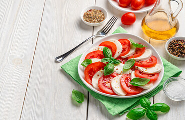 Delicious caprese salad with ripe tomatoes and mozzarella cheese, basil and olive oil on a white background. Italian cuisine.