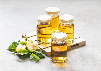 Fresh apple juice in small glass bottles with lids on a wooden pallet on a light gray background