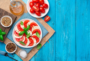 Italian caprese salad with sliced tomatoes, mozzarella cheese and fresh basil leaves on a blue wooden background.