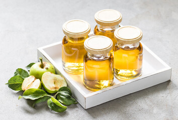 Natural green apple juice in small glass bottles with lids in a wooden box on a light gray background