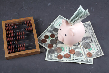 pig piggy bank stands on one-dollar bills next to mechanical bills against a dark concrete background.