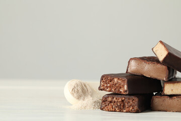 Pieces of tasty bars and spoon with protein powder on white table. Space for text