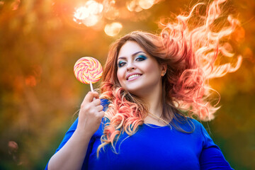 Happy plus size model with big lollipop outdoors, fat woman in autumn park among yellow leaves