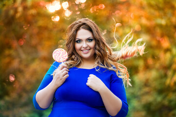 Happy plus size model with big lollipop outdoors, fat woman in autumn park among yellow leaves