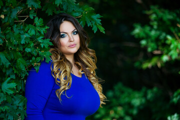 Naklejka premium Happy plus size model in blue dress outdoors, fat woman in autumn park among yellow leaves