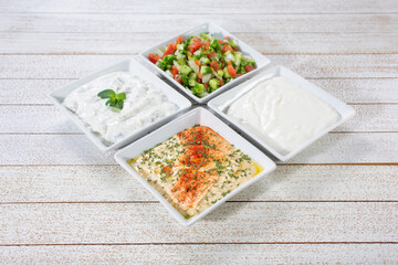 A view of a collection of Persian side dishes featuring hummus, shirazi, mast-o-musir and mast-o-kheyar.