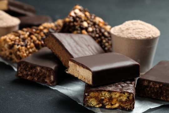 Different tasty energy bars and protein powder on black table, closeup