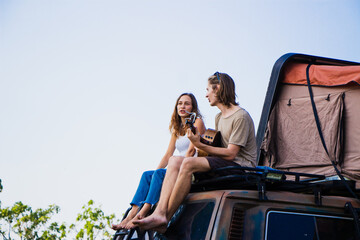 Fototapeta na wymiar Young man and woman having fun and playing guitar and singing while summer vacation camping.
