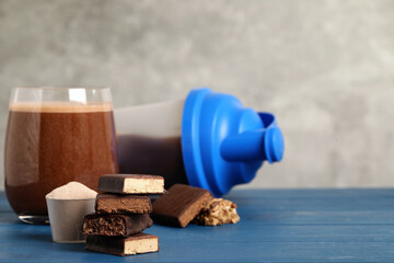Different energy bars, protein cocktail and powder on blue wooden table. Space for text