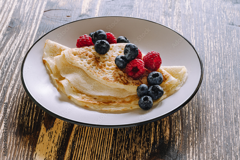 Wall mural Crepes with berries on wooden background