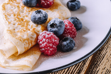Crepes with berries on wooden background