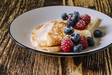 Crepes with berries on wooden background