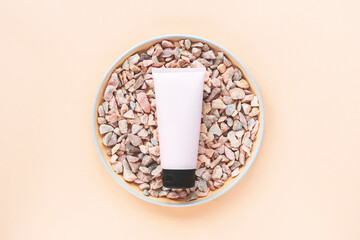 Cosmetic unbranded cream tube on natural stones on beige background. Top view, flat lay. Mock up