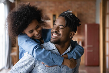 Happy loving millennial African American couple hug embrace show care affection in family relations. Smiling young ethnic woman piggyback excited biracial man, excited moving relocating together.