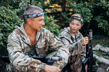 Father and son in camouflage ready to play in laser tag shooting game with a weapon outdoor