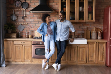 Overjoyed millennial African American man and woman laugh joke relax together in renovated design...