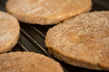 four frozen hamburgers on the grill. Frozen fast food.