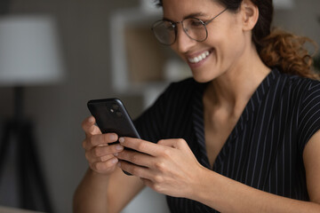 Close up smiling woman in glasses using smartphone, browsing mobile device apps, chatting with...