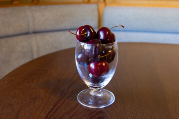 The transparent glass is filled with a large ripe beautiful cherry