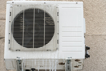 An outdoor air conditioner unit installed on the outer wall of a residential building close-up. Operation of the air conditioner in winter at low temperatures. Icicles and snow on the air conditioner