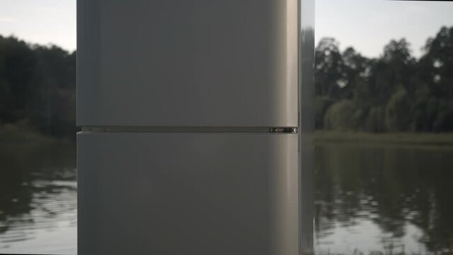 Elegant closed domestic refrigerator demonstrated on bank of tranquil lake against forest on summer day closeup