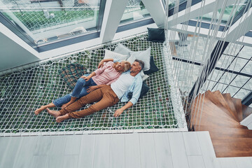 Top view of beautiful mature couple smiling and communicating while relaxing in big hammock at home...