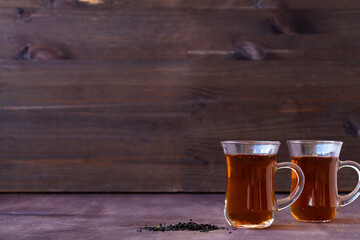 Turkish tea in traditional glass on the wooden table close-up. two glass cups of black tea with dry leaves on the dark brown background with copy space.