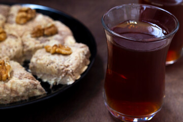 close-up sunflower halva with fork and Turkish tea in traditional glass on the wooden table close-up. glass cup of black tea with walnuts on the dark brown background with copy space.Turkish desserts.
