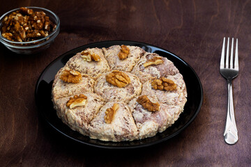 sunflower halva with fork and Turkish tea in traditional glass on the wooden table close-up. glass cup of black tea with walnuts on the dark brown background with copy space. Turkish desserts.