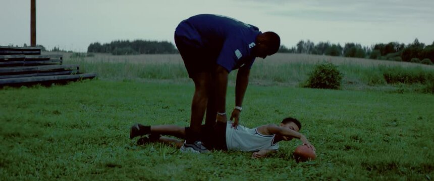 HANDHELD African American father and son playing football together on a lawn in front of their house in the evening. Shot with 2x anamorphic lens