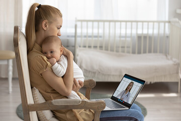 Young Caucasian mother sit in chair hold baby infant in arms speak on video call with pediatrician....