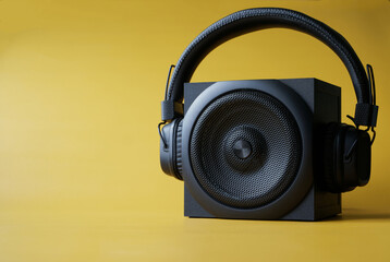 Headphones with ear pads and a black single-band audio speaker on a yellow background. Pop music...