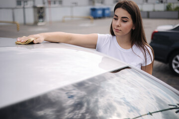 Attractive happy joyful female driver wipe windshield on her car using rag in self-service car wash