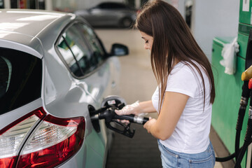 Attractive young woman refueling car at gas station. Female filling diesel at gasoline fuel in car using a fuel nozzle. Petrol concept. Side view - obrazy, fototapety, plakaty