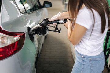 Attractive young woman refueling car at gas station. Female filling diesel at gasoline fuel in car...