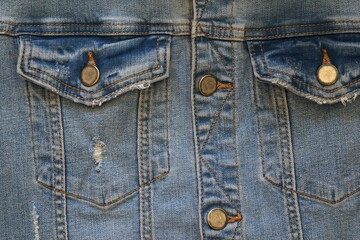 Fototapeta premium the front part with the upper pockets of an old or worn blue denim jacket is a closeup