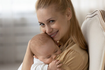 Close up portrait of happy young Caucasian mother hold in arms cuddle lull small baby infant son or daughter. Smiling mom comfort hug little newborn kid child show love care. Motherhood concept.