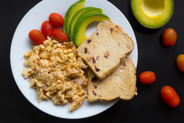 Breakfast dish with omet, bread, tomato and avocado sliced.
