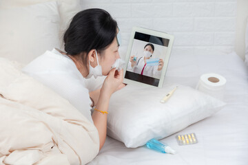 Woman patient examines body temperature during consultation with smart doctor. Sick woman in bed video call to doctor using tablet. Concept of home isolation telemedicine and patient counseling online