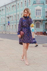 Young beautiful woman in blue dress with a round bag walking on the spring street. Urban background. Stylish Tourist girl enjoying walking the city during weekend trip.