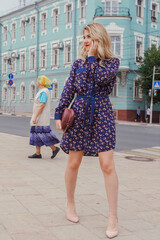 Young beautiful woman in blue dress with a round bag walking on the spring street. Urban background. Stylish Tourist girl enjoying walking the city during weekend trip.