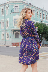 Naklejka premium Young beautiful woman in blue dress with a round bag walking on the spring street. Urban background. Stylish Tourist girl enjoying walking the city during weekend trip.