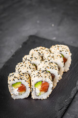 appetizing california sushi roll with cheese avocado cucumber and salmon in sesame seeds on a black stone plate