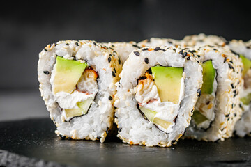 appetizing sushi roll california with eel avocado cucumber and sesame seeds on a black stone plate